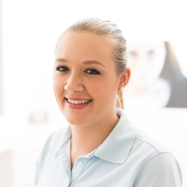 Porträt von Anja Frenzel vor einem unscharfen Hintergrund. Sie trägt ein hellblaues Polo-Shirt und lächelt freundlich in die Kamera