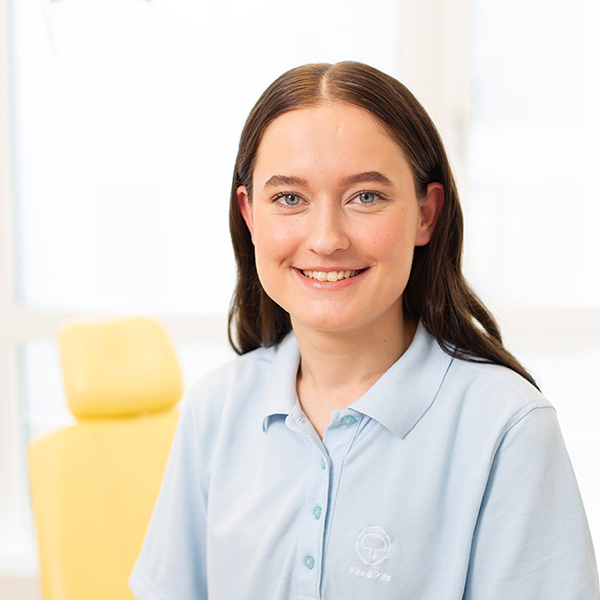 Porträt von Eldina Uslu vor einem unscharfen Hintergrund. Sie trägt ein hellblaues Polo-Shirt und lächelt freundlich in die Kamera