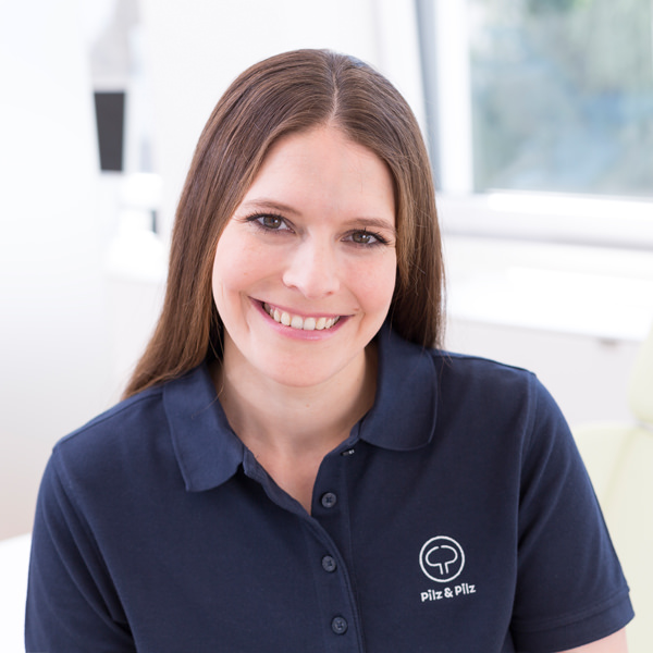 Porträt von Dr. Lena Pilz vor einem unscharfen Hintergrund. Sie trägt ein dunkelblaues Polo-Shirt mit weiß aufgesticktem Pilz-&-Pilz-Logo und lächelt freundlich in die Kamera