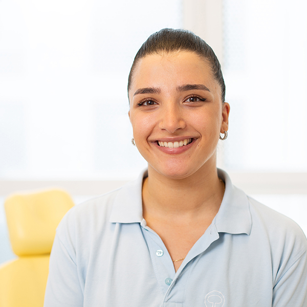 Porträt von Nadire Uslu vor einem unscharfen Hintergrund. Sie trägt ein hellblaues Polo-Shirt und lächelt freundlich in die Kamera